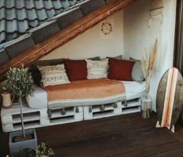 a pallet bench with cushions is fitted neatly under a low roof on a balcony