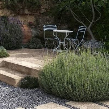 a raised stone patio with furniture, in a gravel garden with several huge lavender shrubs