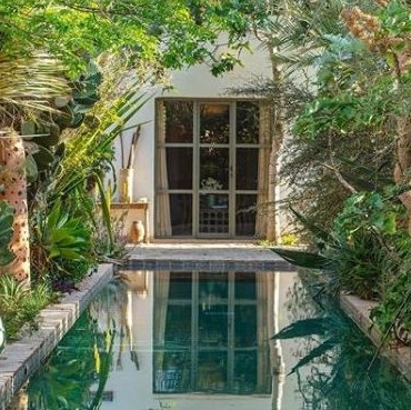 a traditional Moroccan garden with a long, blue pool running down the middle and lots of plants either side